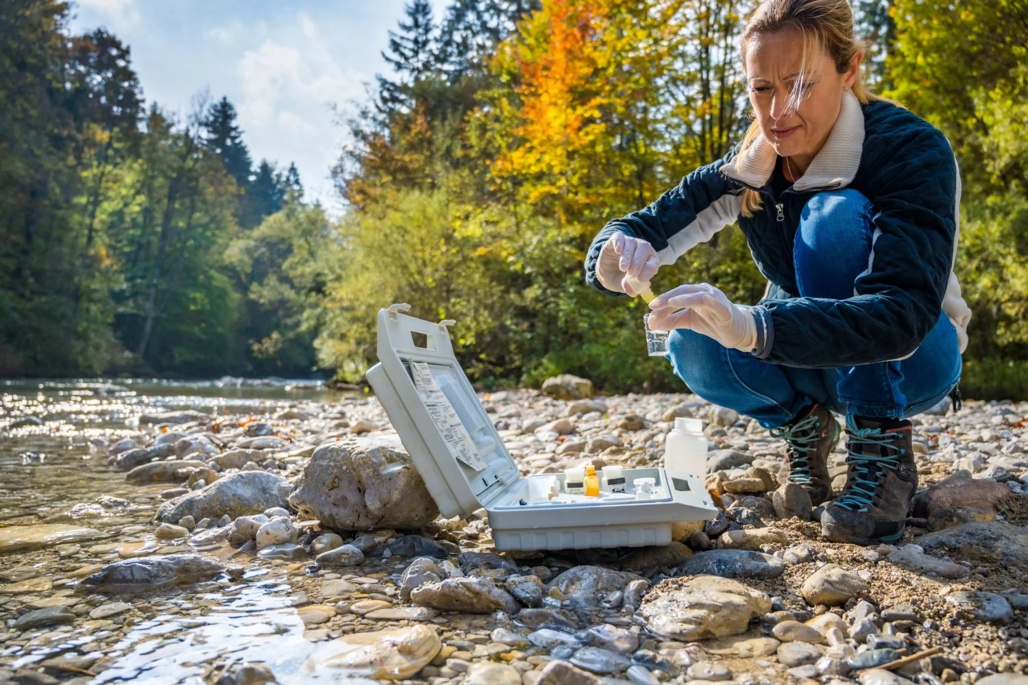 Mitarbeiterin des Umweltlabors entnimmt Wasserprobe aus Fluss im Rahmen einer umwelttechnischen Untersuchung